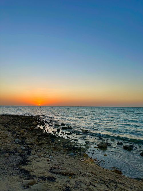 Free A tranquil sunset over the ocean with a rocky shore, perfect for relaxation themes. Stock Photo