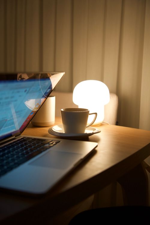 Free A serene workspace with a laptop and a coffee mug illuminated by a warm lamp. Stock Photo