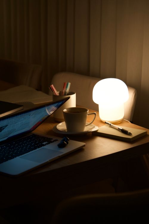 Free Warmly lit workspace featuring a laptop, lamp, and coffee cup, creating a cozy and productive atmosphere. Stock Photo
