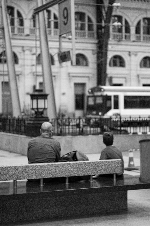 Free Black and white urban scene with two people sitting watching a tram pass by. Stock Photo