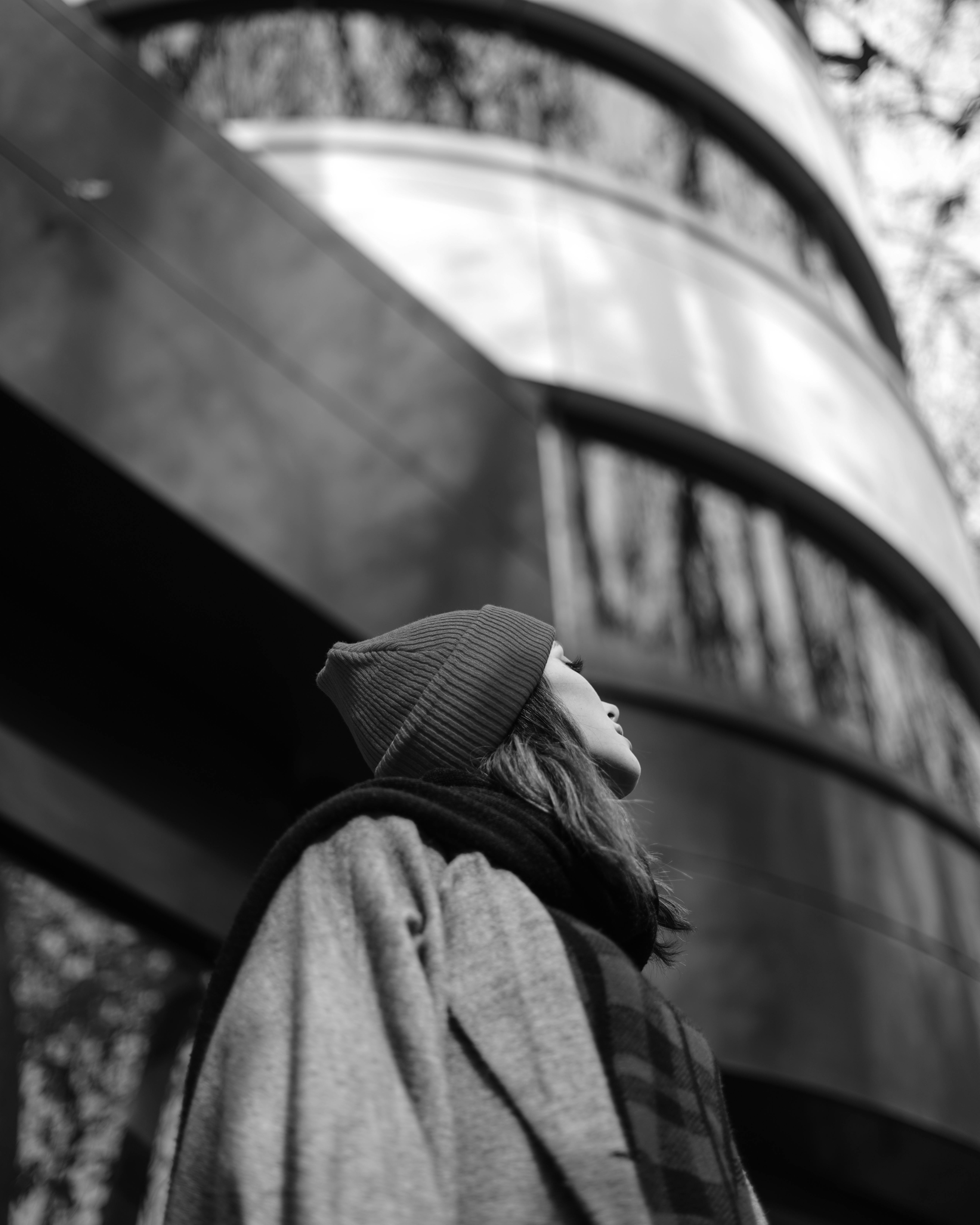 A woman in a beanie gazes thoughtfully in a modern urban setting.