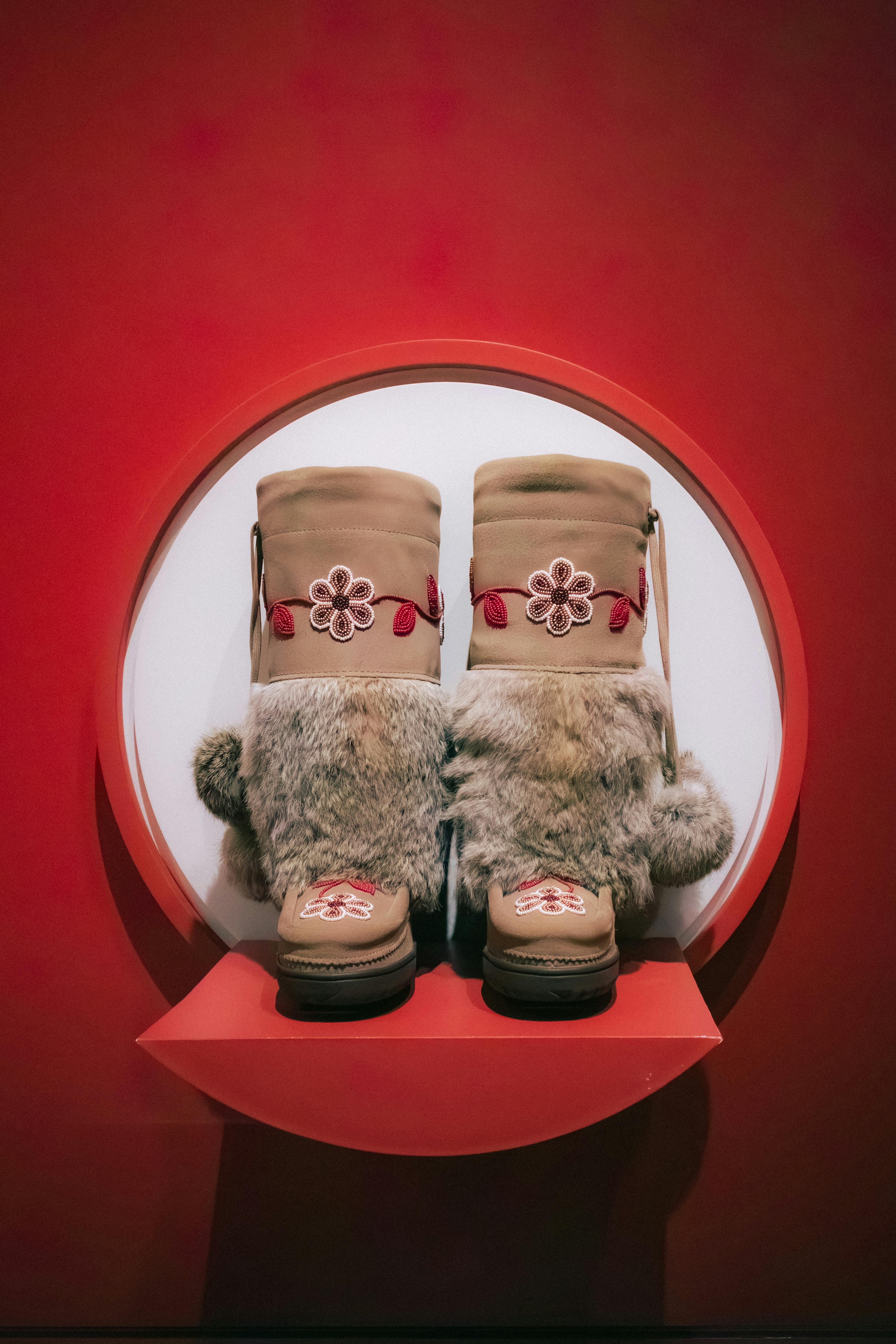 Artful display of traditional fur boots in a Toronto art museum against a red background.