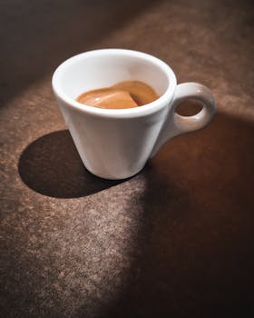 A simple espresso cup casting a shadow on a rustic surface, highlighting natural light and minimalism.