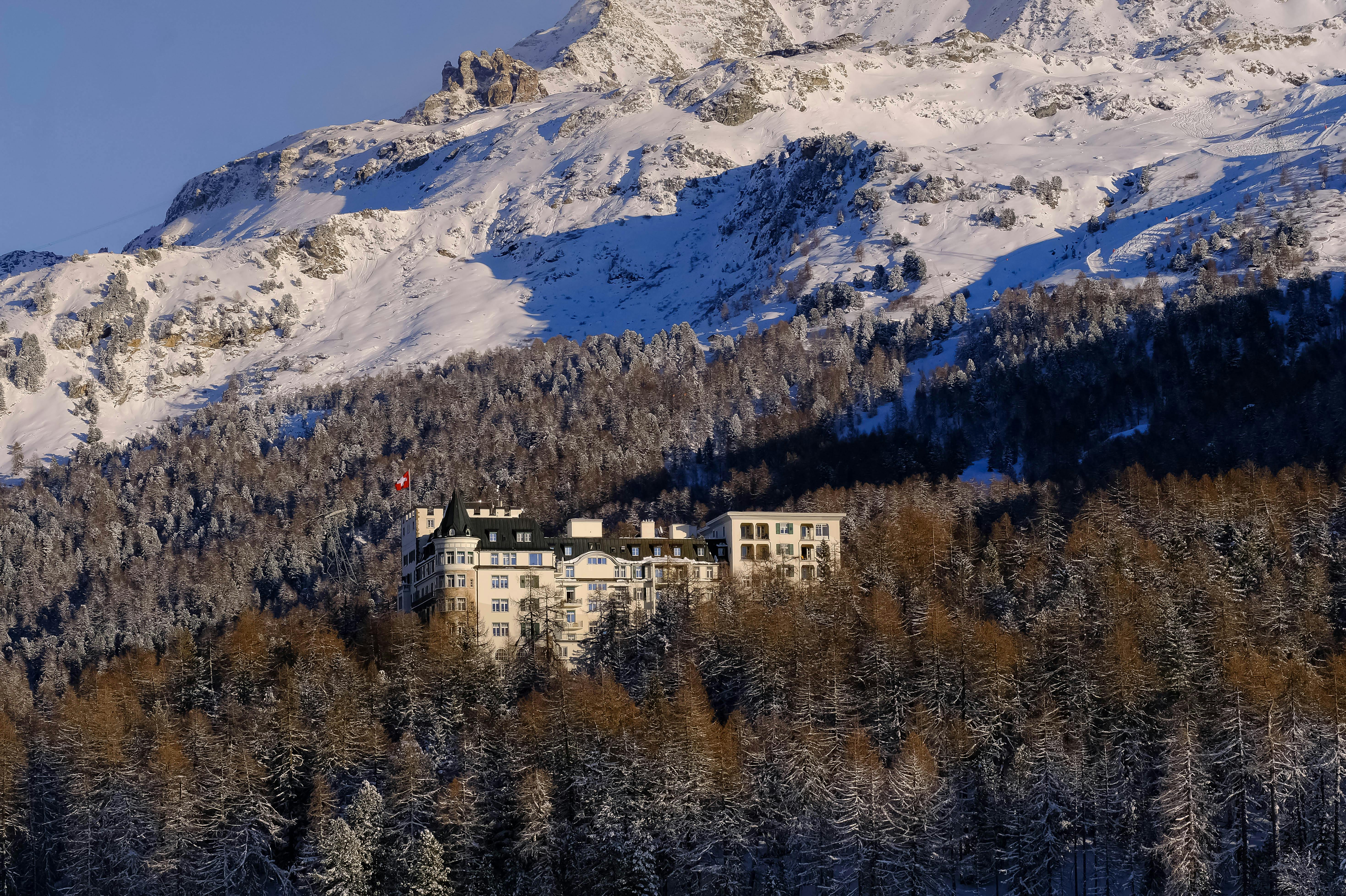 A scenic view of a luxurious hotel nestled in snow-covered alpine mountains amidst a dense winter forest.
