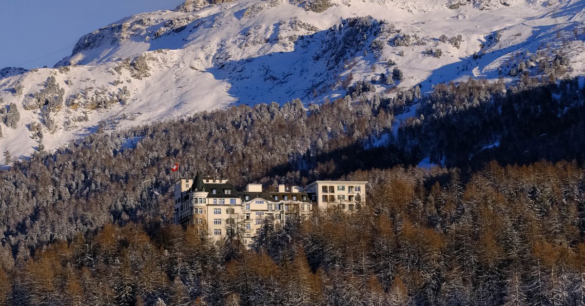 A scenic view of a luxurious hotel nestled in snow-covered alpine mountains amidst a dense winter forest.