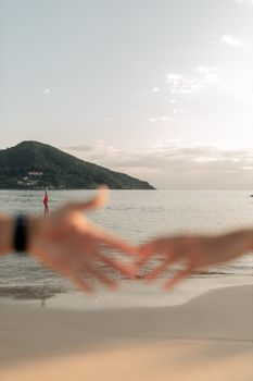 Blurred hands reaching together on serene beach with island backdrop, creating a romantic atmosphere.