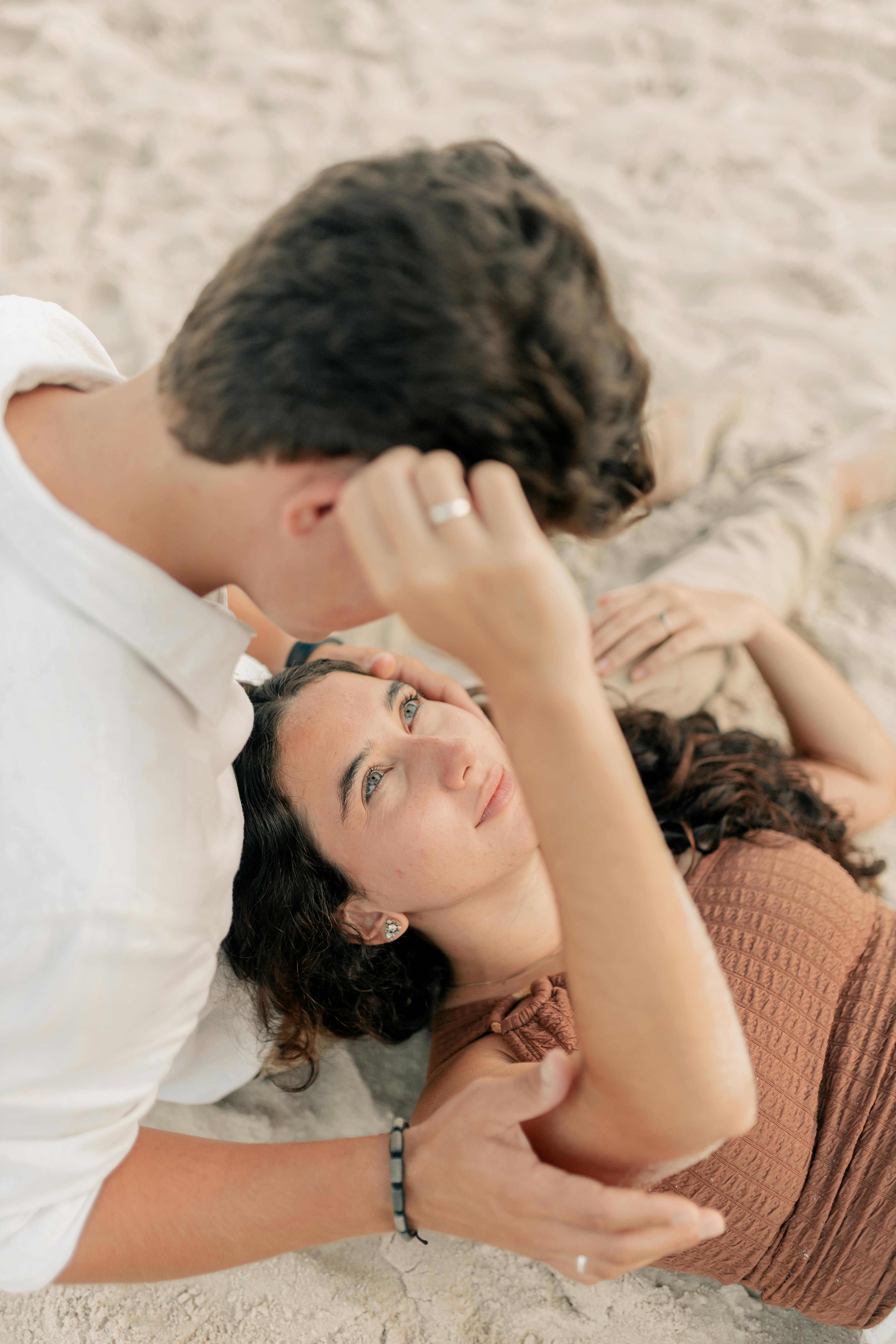 A couple shares a tender moment while lounging on a sandy beach, exuding warmth and love.