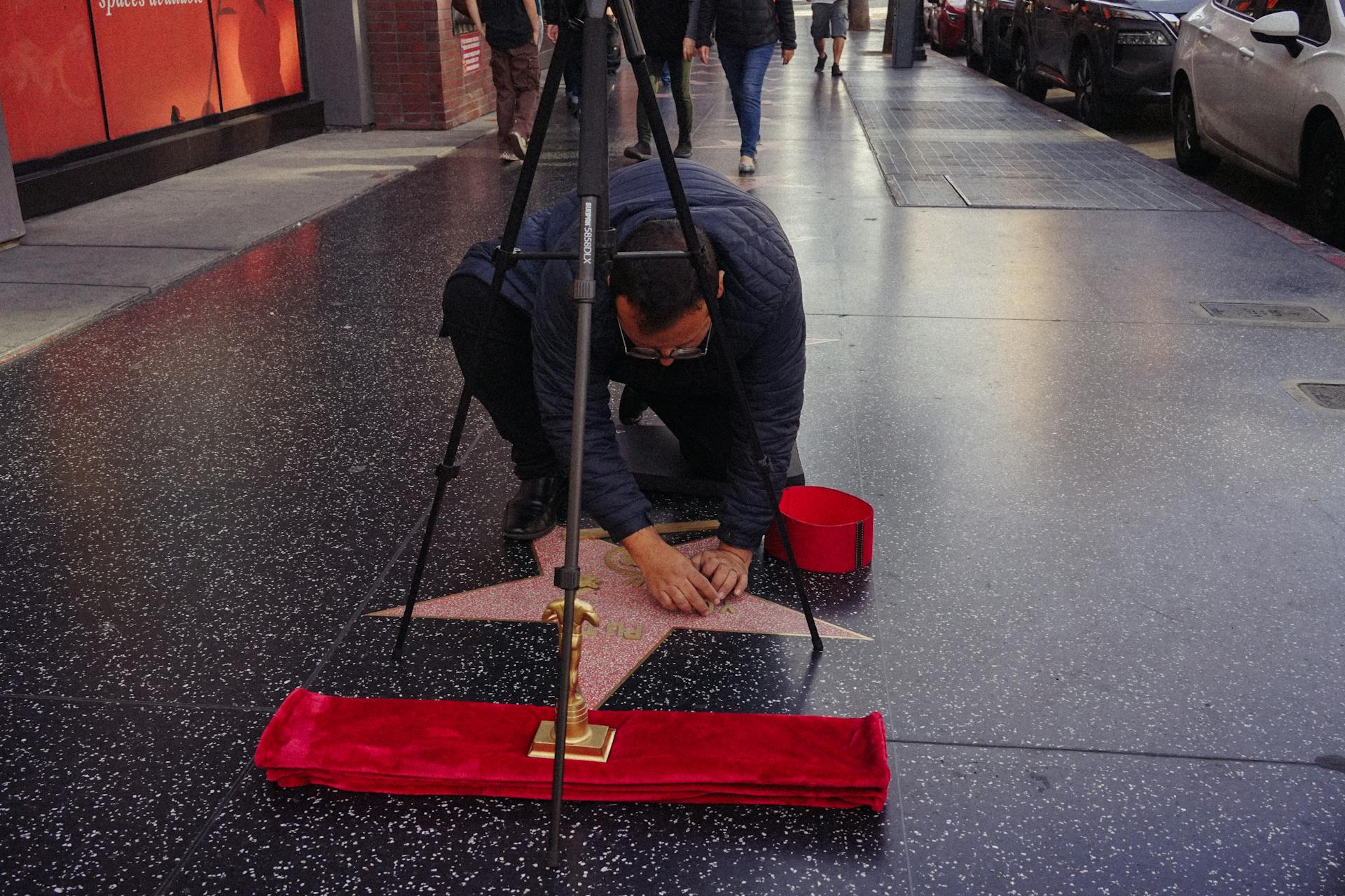 A man meticulously cleans a star on the Hollywood Walk of Fame, symbolizing celebrity culture.