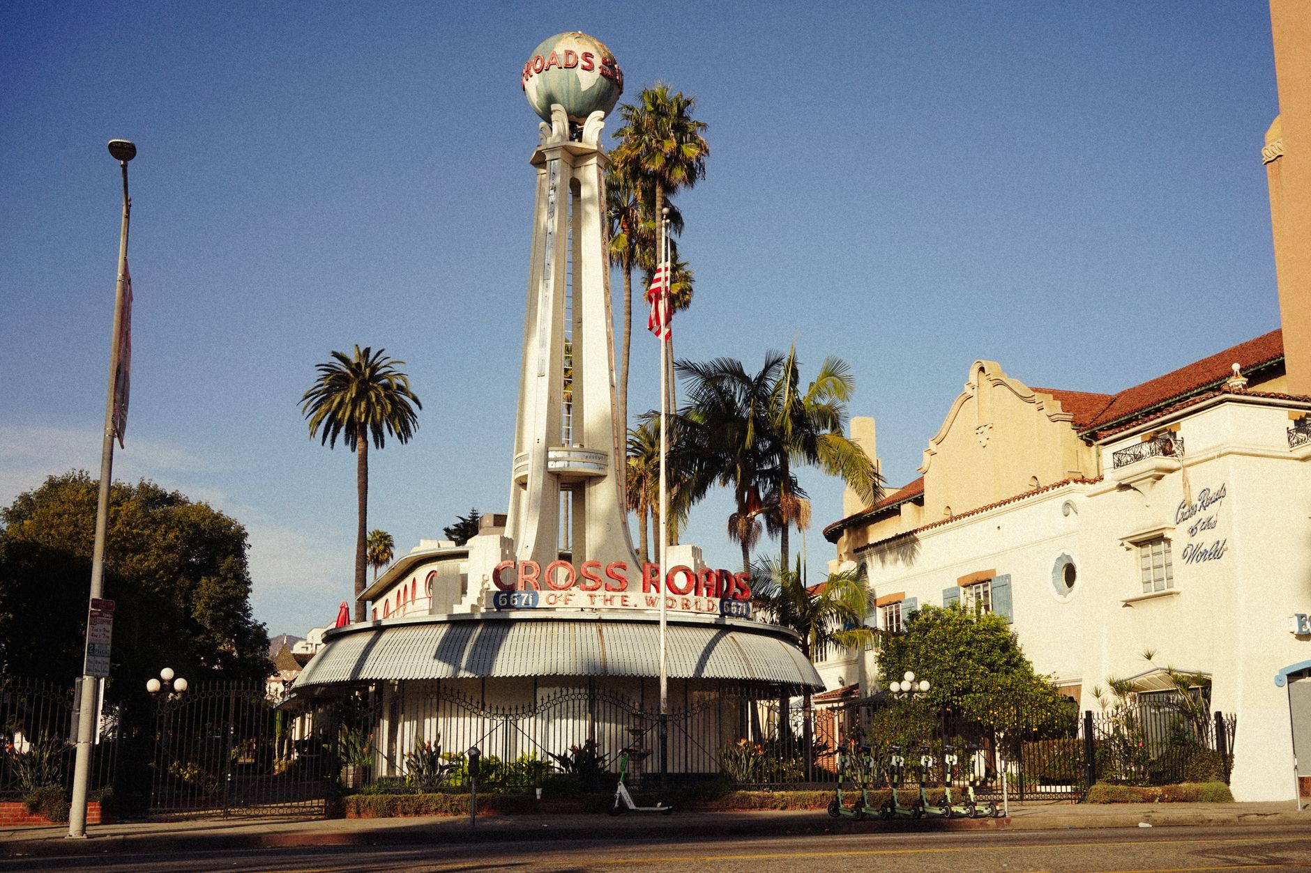 Vintage view of the iconic Crossroads of the World landmark in Los Angeles, featuring palm trees under a clear sky.