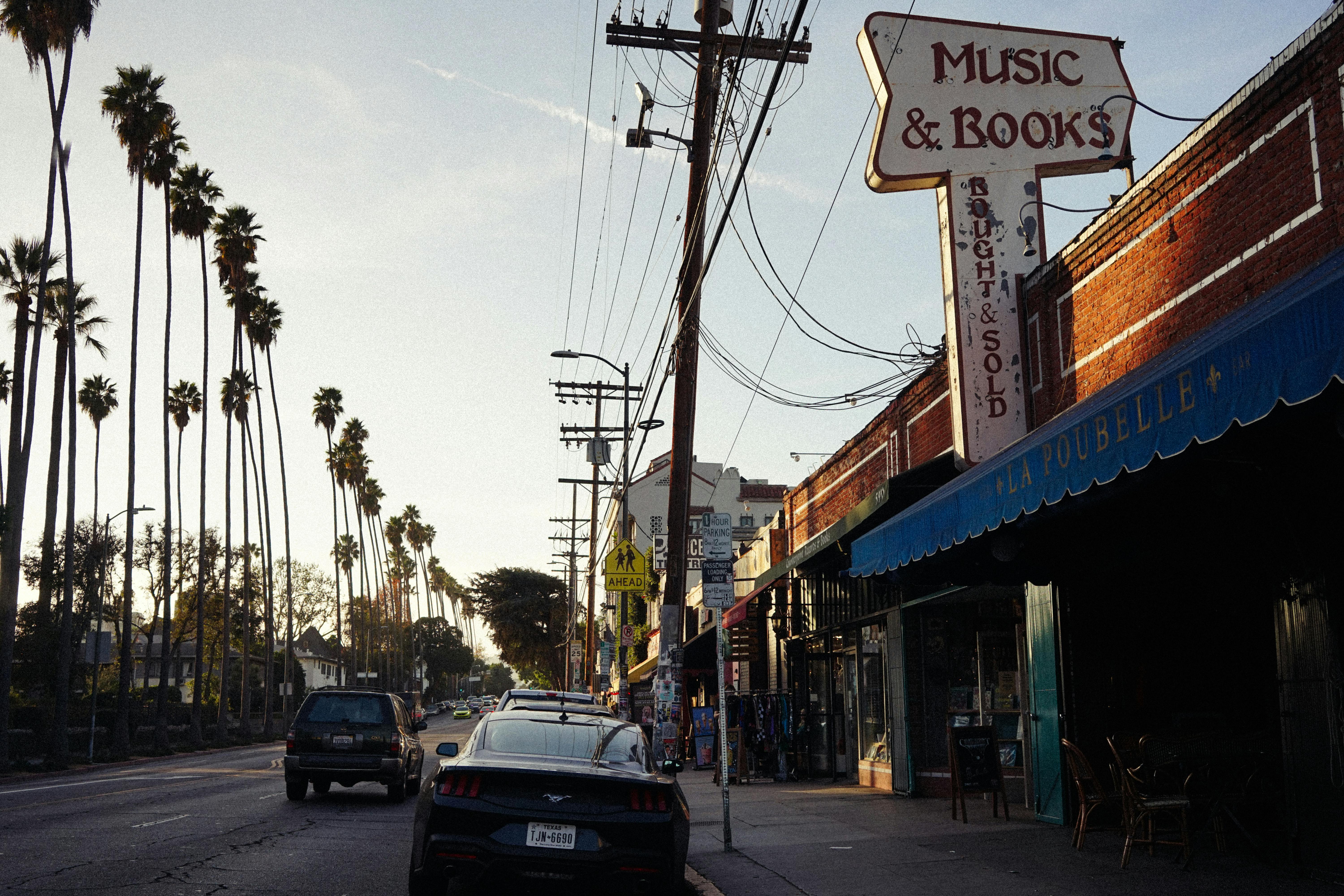 Free Charming street view at sunset with palm trees and a vintage bookstore in an urban setting. Stock Photo