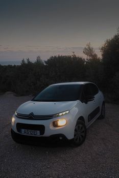 A compact white car parked on a gravel path at twilight surrounded by nature.