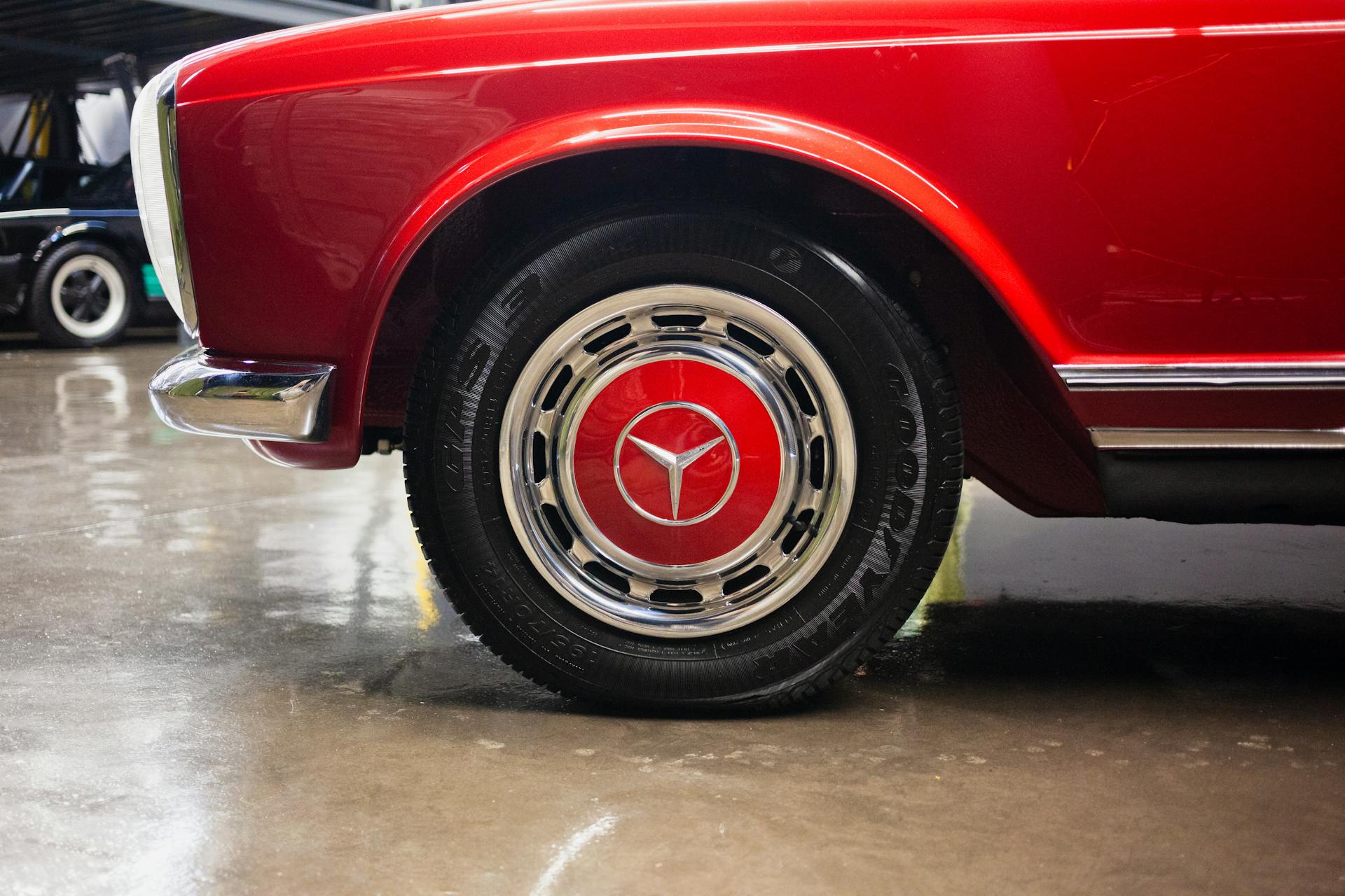 Detailed photo of the front wheel of a vintage red car showcasing the hubcap and tire details.