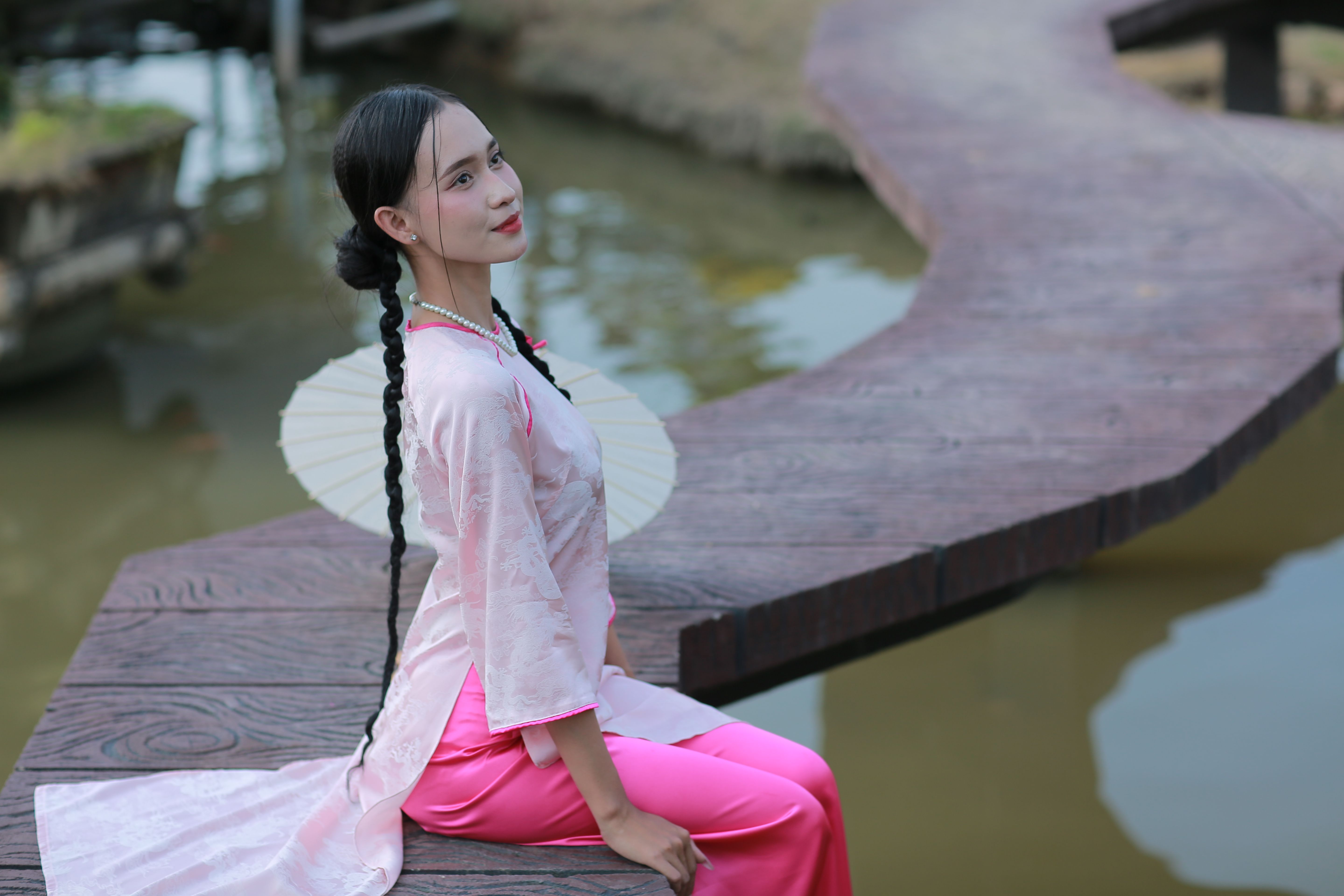 A woman in traditional attire sitting by the water on a wooden walkway.