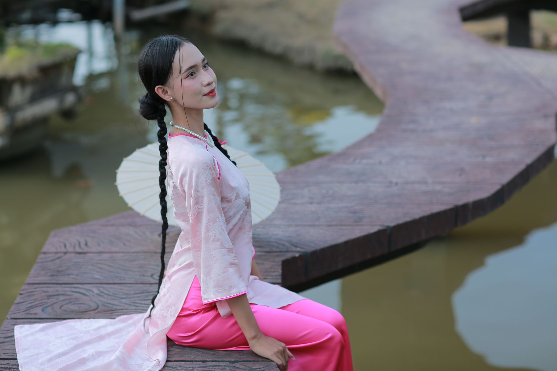 A woman in traditional attire sitting by the water on a wooden walkway.