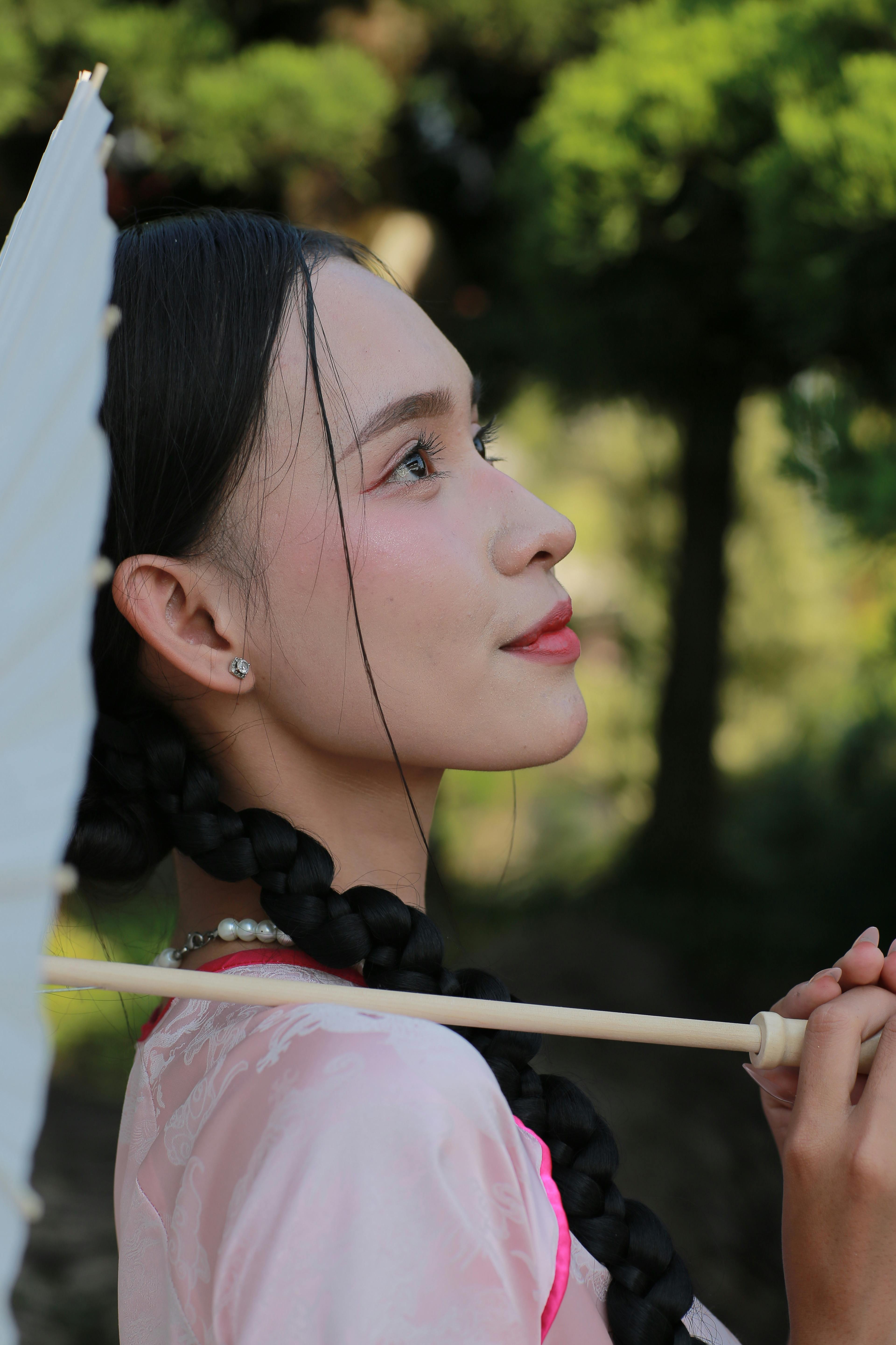 Side profile of a woman with braided hair holding a traditional umbrella in a serene outdoor setting.