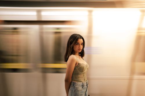 Free Portrait of a young woman standing confidently in front of a blurred moving train, day setting. Stock Photo