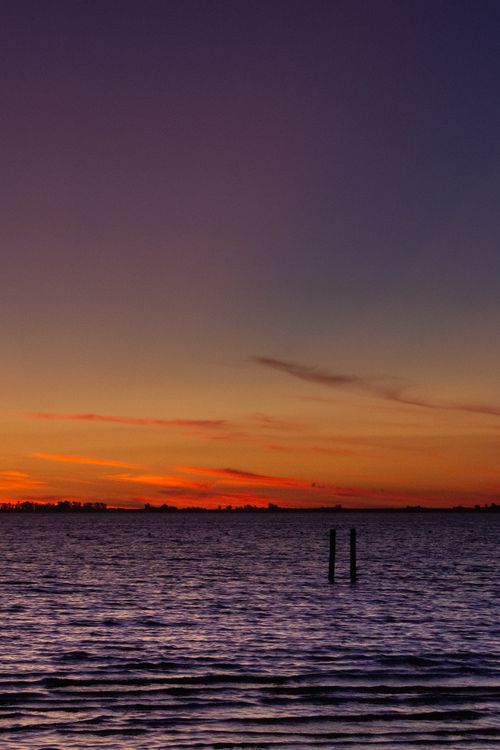 Free Beautiful sunset over calm ocean waters with vibrant orange and purple hues. Stock Photo