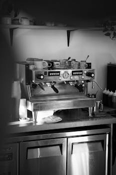 Black and white photo of an espresso machine in a cozy café. Ideal for coffee-themed visuals.