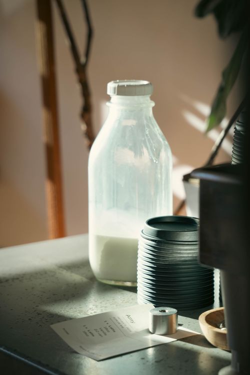 Free A warm, sunlit café table with a bottle of milk and stacked cups for a cozy ambiance. Stock Photo