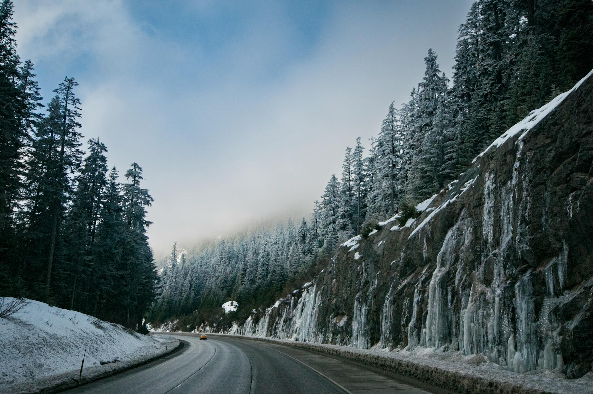 Captivating winter road winding through snow-covered forest and icy cliffs under a clear sky.