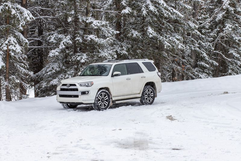 White SUV parked in a snow-covered forest, showcasing winter driving conditions and landscape.