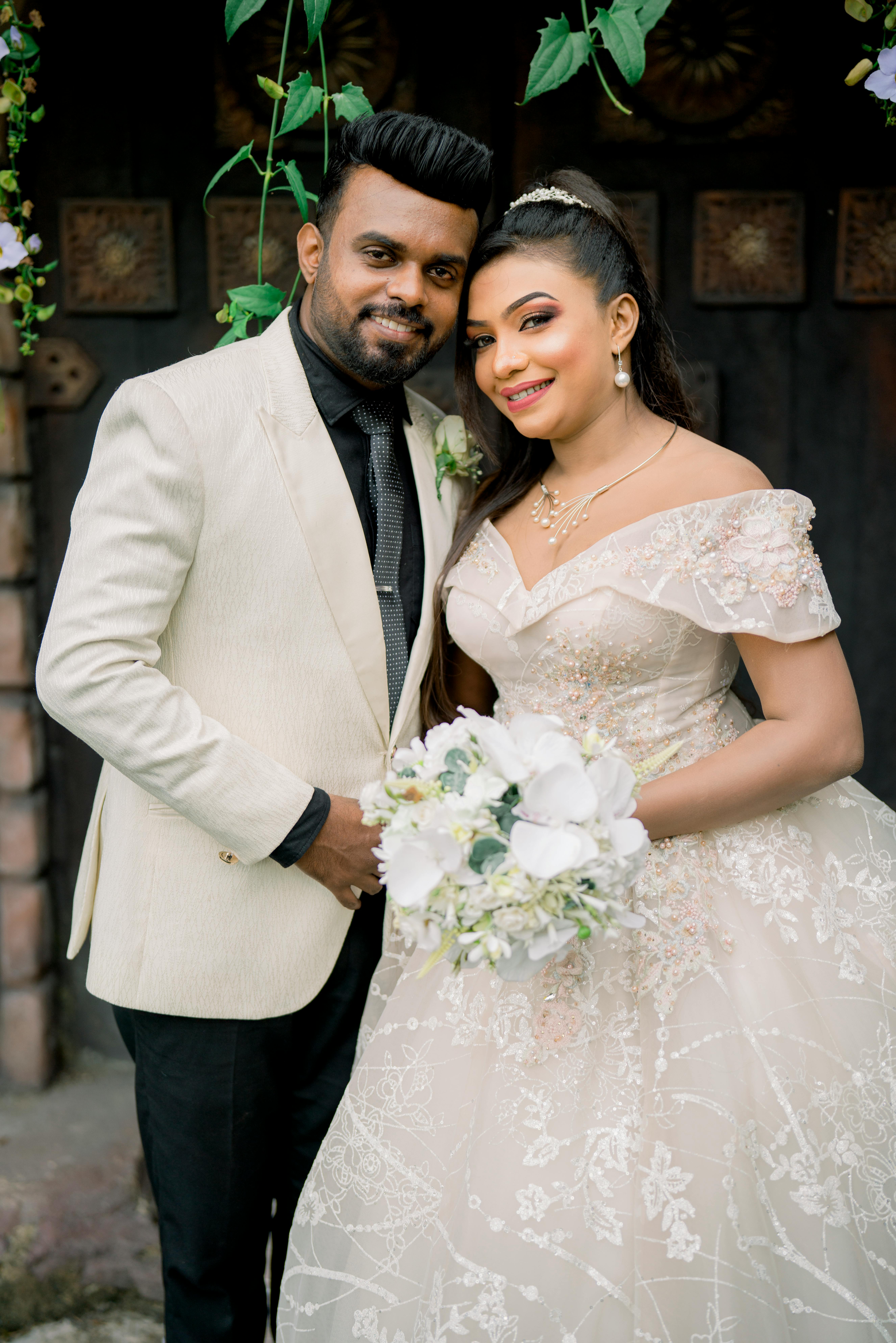 Charming couple in wedding attire posing outdoors with floral arrangement.