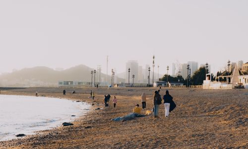 Free People enjoying a tranquil beach walk at sunset with city skyline views. Stock Photo