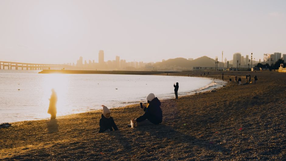 Peaceful dusk on a city beach with people enjoying the serene shoreline and urban skyline in the background.