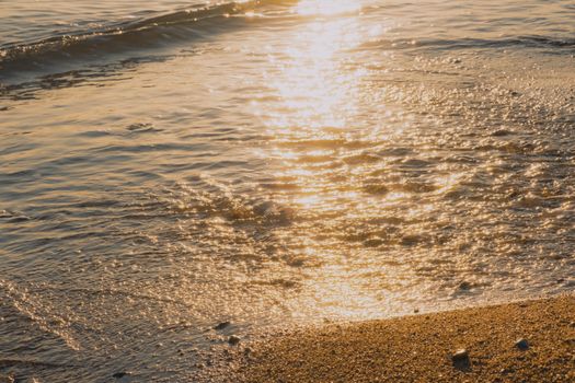Sunset sunlight reflecting on a tranquil sandy beach, creating a serene and warm atmosphere.
