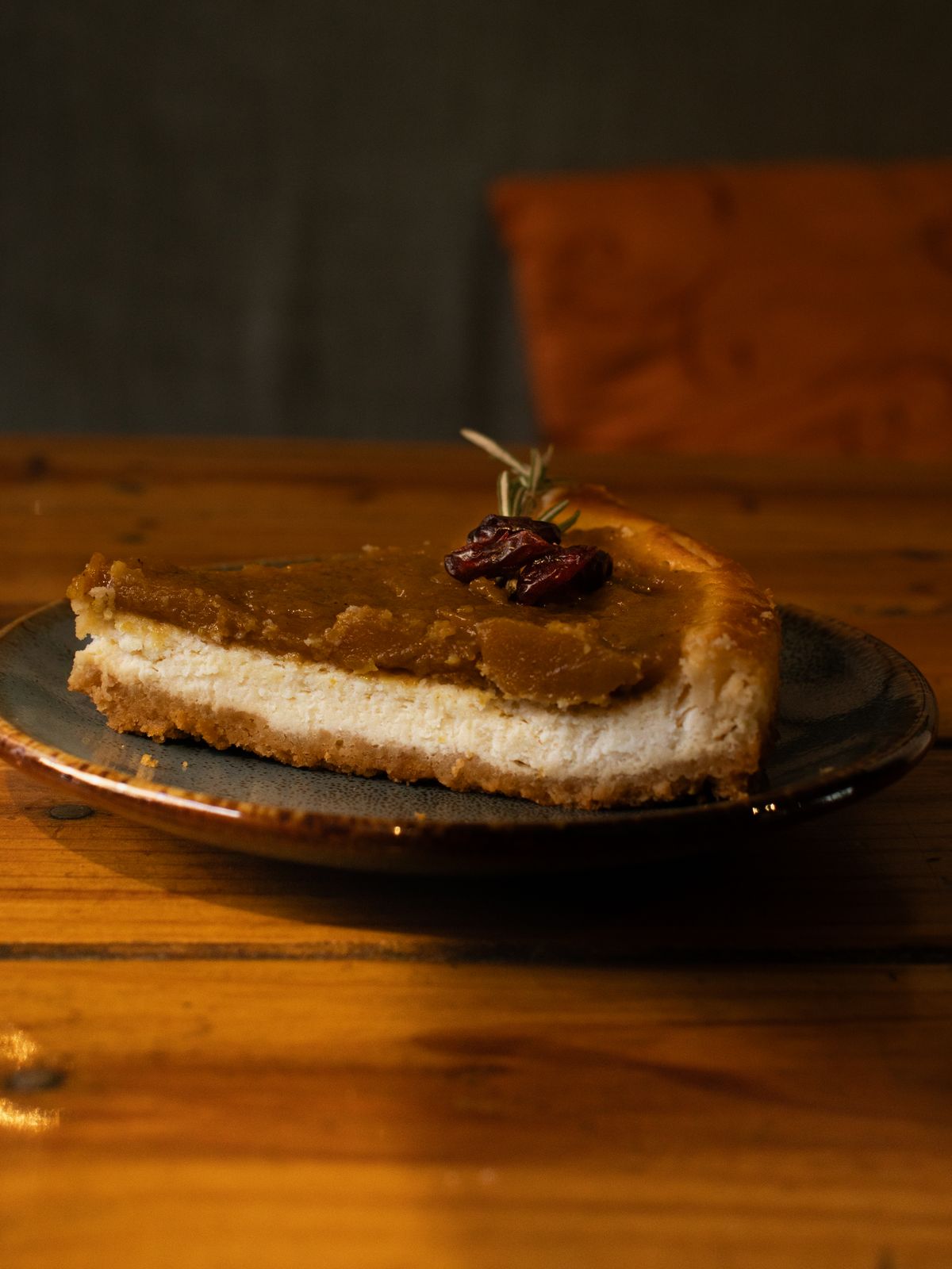 A slice of pumpkin cheesecake with a golden crust and cranberry garnish on a rustic plate