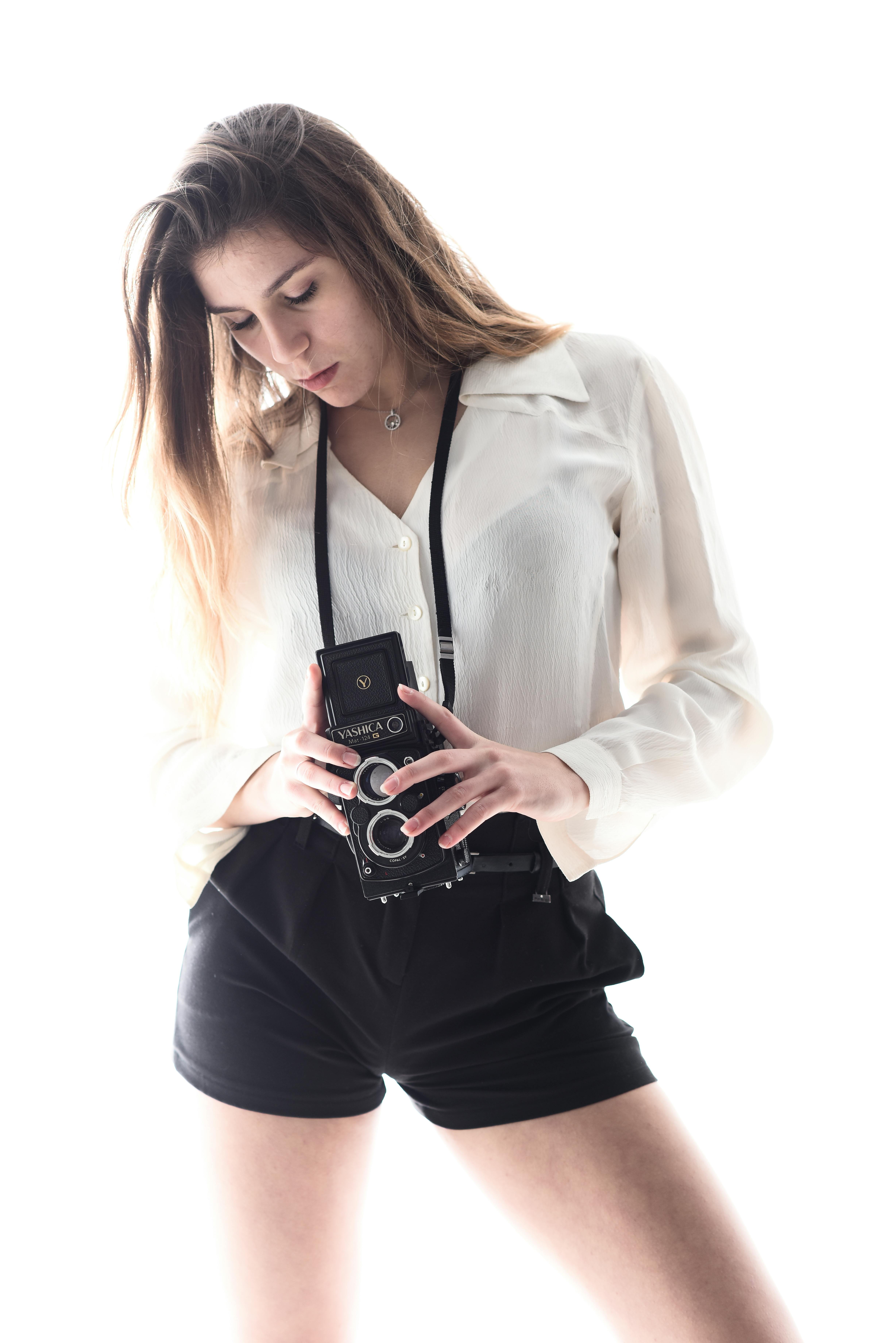 gratis Een jonge vrouw in een wit bloesje houdt een vintage camera vast in een fotosetting met een hoge focus. Stockfoto