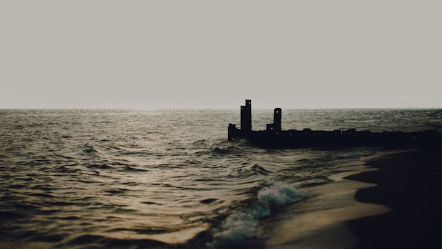Peaceful shoreline at sunset with weathered pier silhouette in the background.