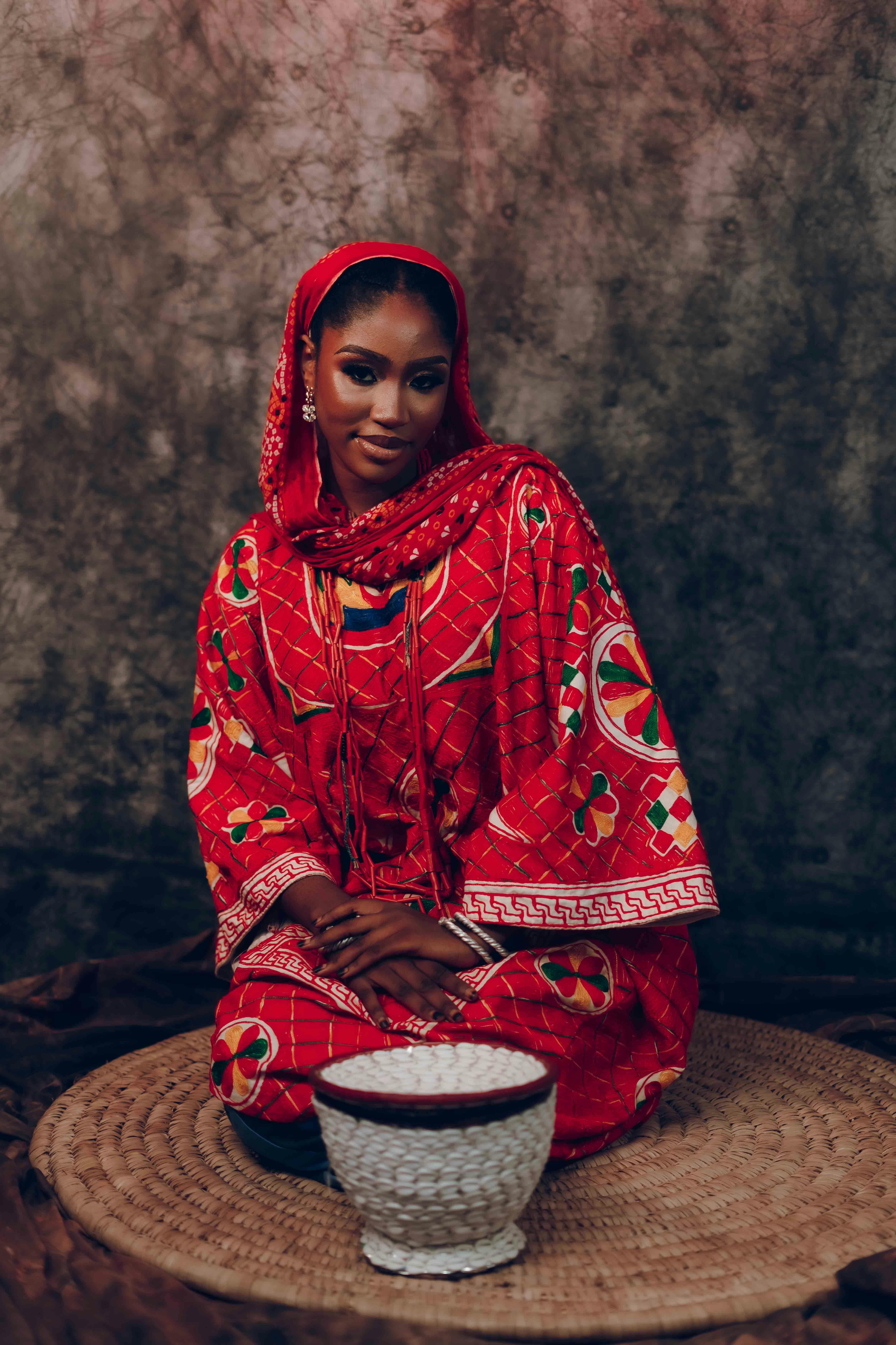 A woman in vibrant red traditional clothing sits gracefully indoors, exuding cultural elegance.