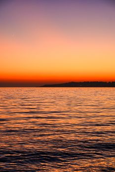 Vivid sunset over serene ocean surface with distant shoreline, creating a breathtaking view.