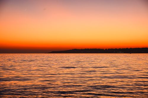 Free Captivating sunset over the ocean with calm waters and a crescent moon in the sky. Stock Photo