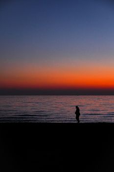 A lone silhouette stands on the beach as the sky glows with vivid sunset colors.