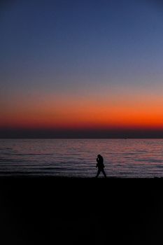 A lone figure's silhouette walks along the beach at sunset, creating a peaceful scene.