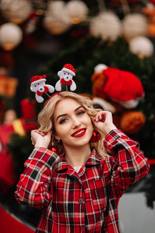 Free Smiling woman in Santa headband and plaid attire at festive outdoor setting. Stock Photo