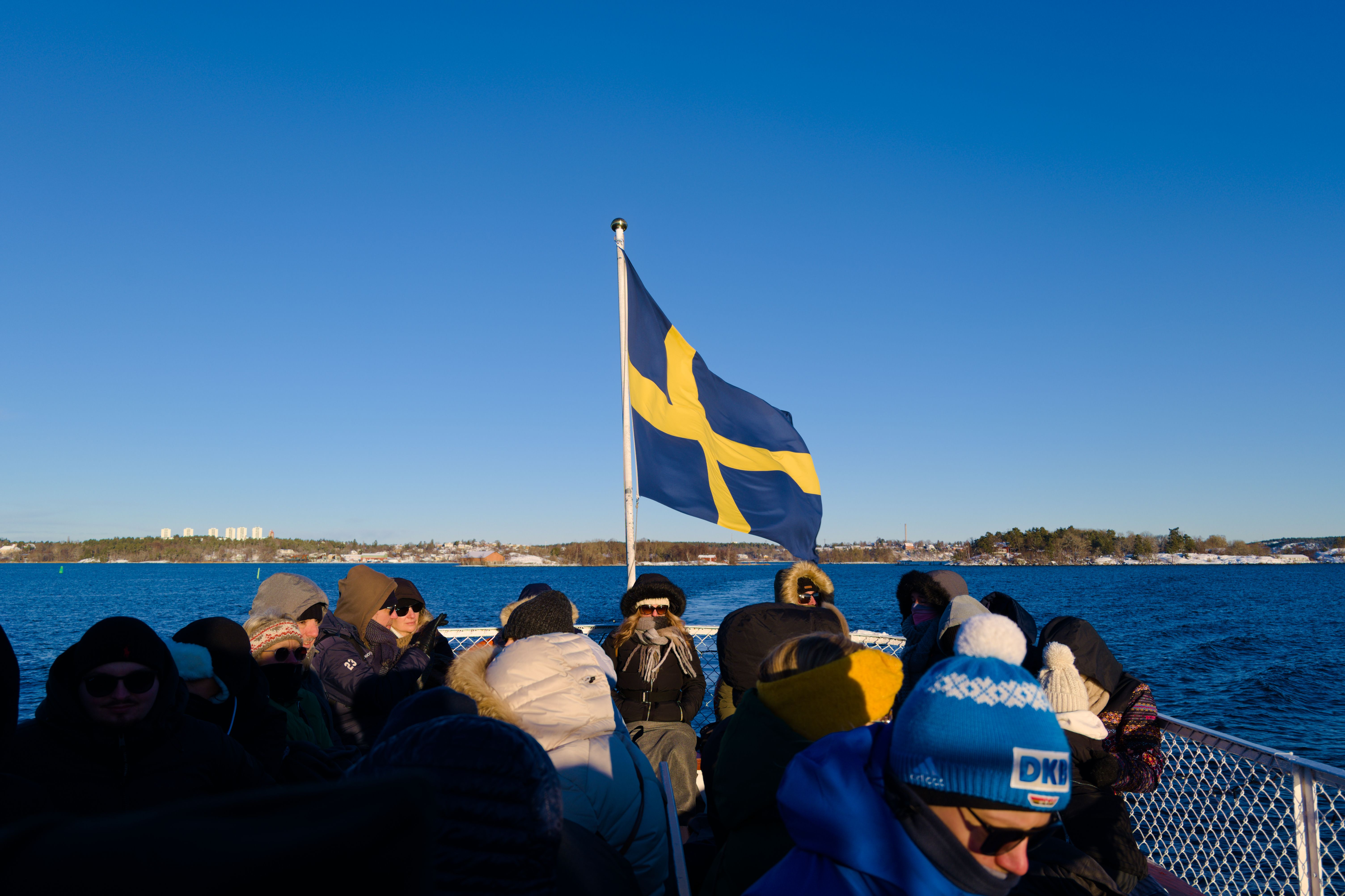 People on a winter boat tour in Stockholm, Sweden with the Swedish flag waving.