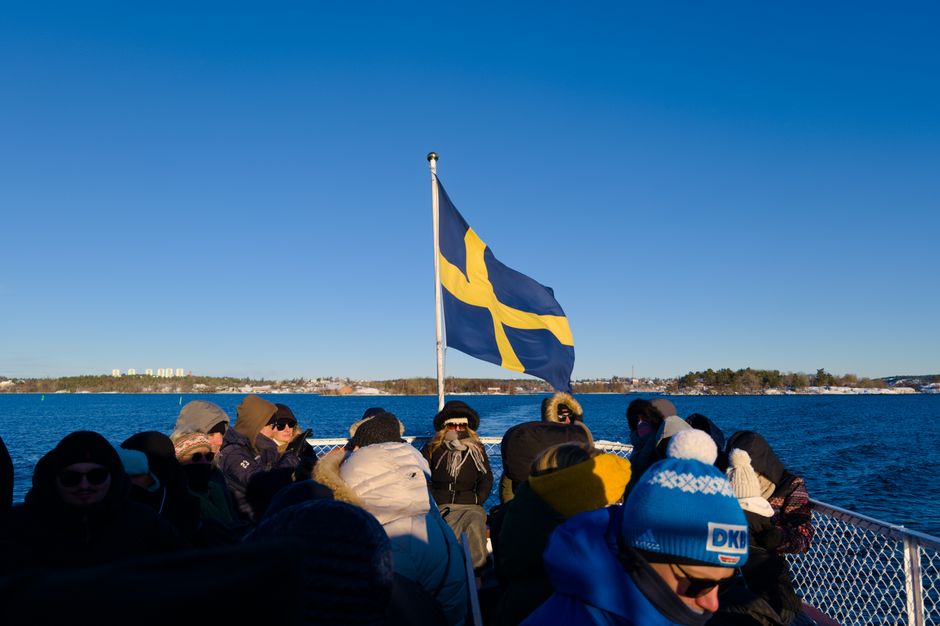 People on a winter boat tour in Stockholm, Sweden with the Swedish flag waving.