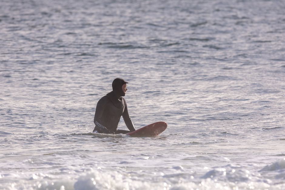 A lone surfer in a wetsuit waits patiently on his surfboard amid calm ocean waters.