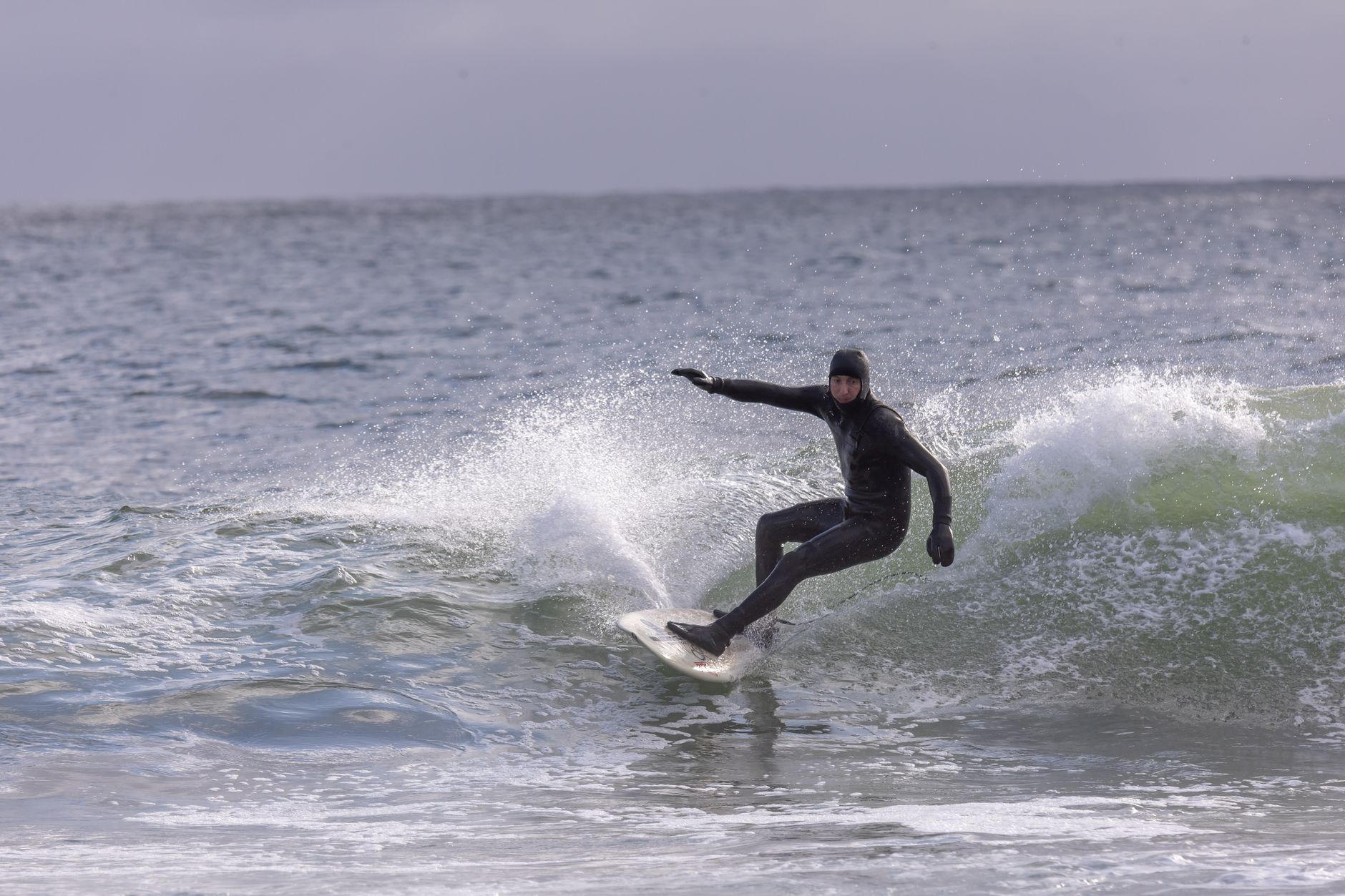 A surfer rides a wave in cold weather wearing a wetsuit in the ocean.