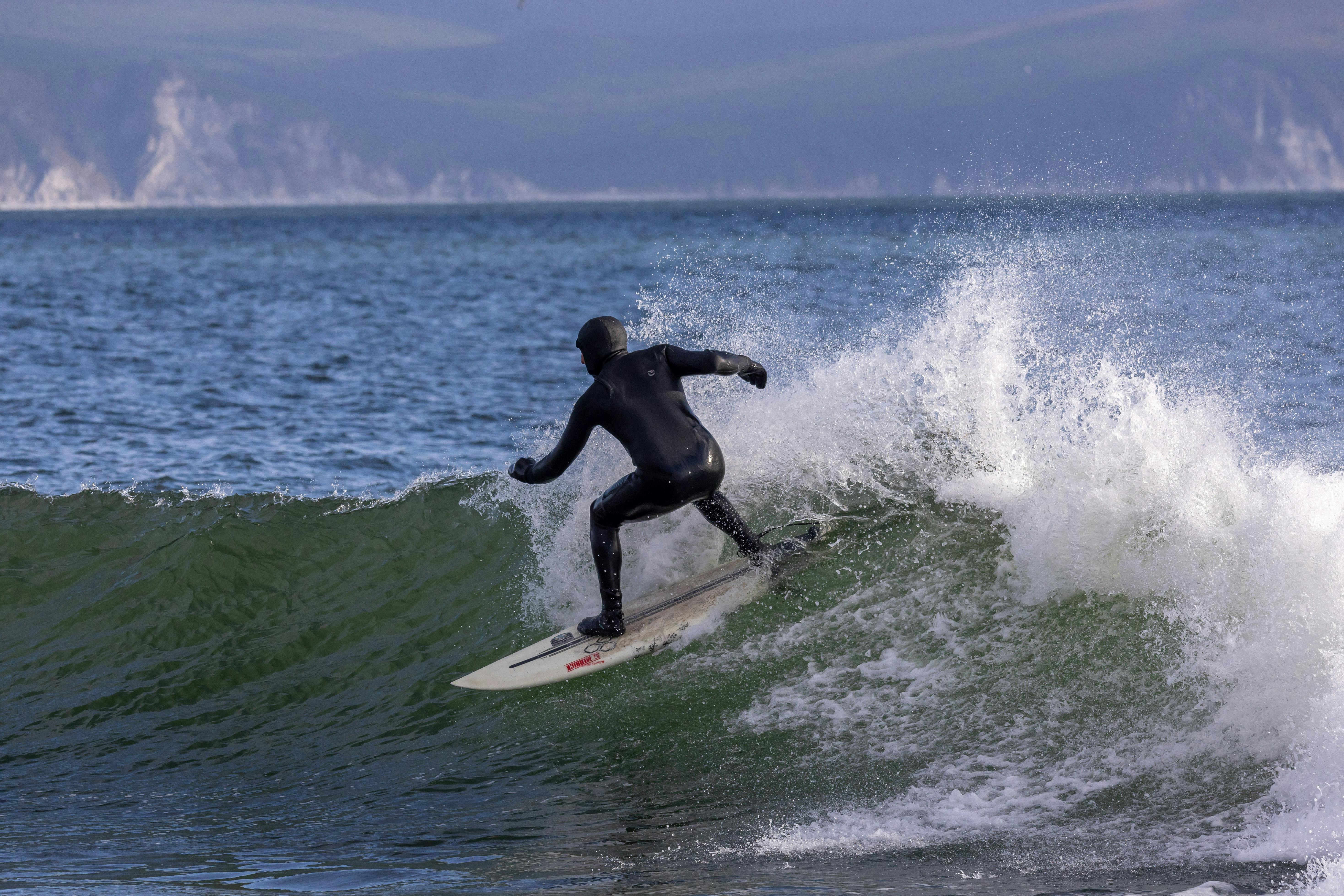 A surfer wearing a wetsuit skillfully rides a wave in the cold ocean waters, showcasing adventurous spirit.