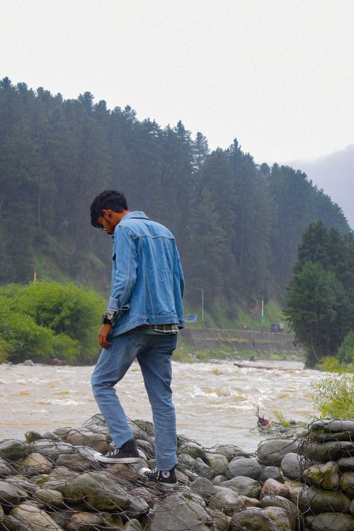 Free A man in denim attire walks by a river in the serene wilderness of Kashmir, India. Stock Photo