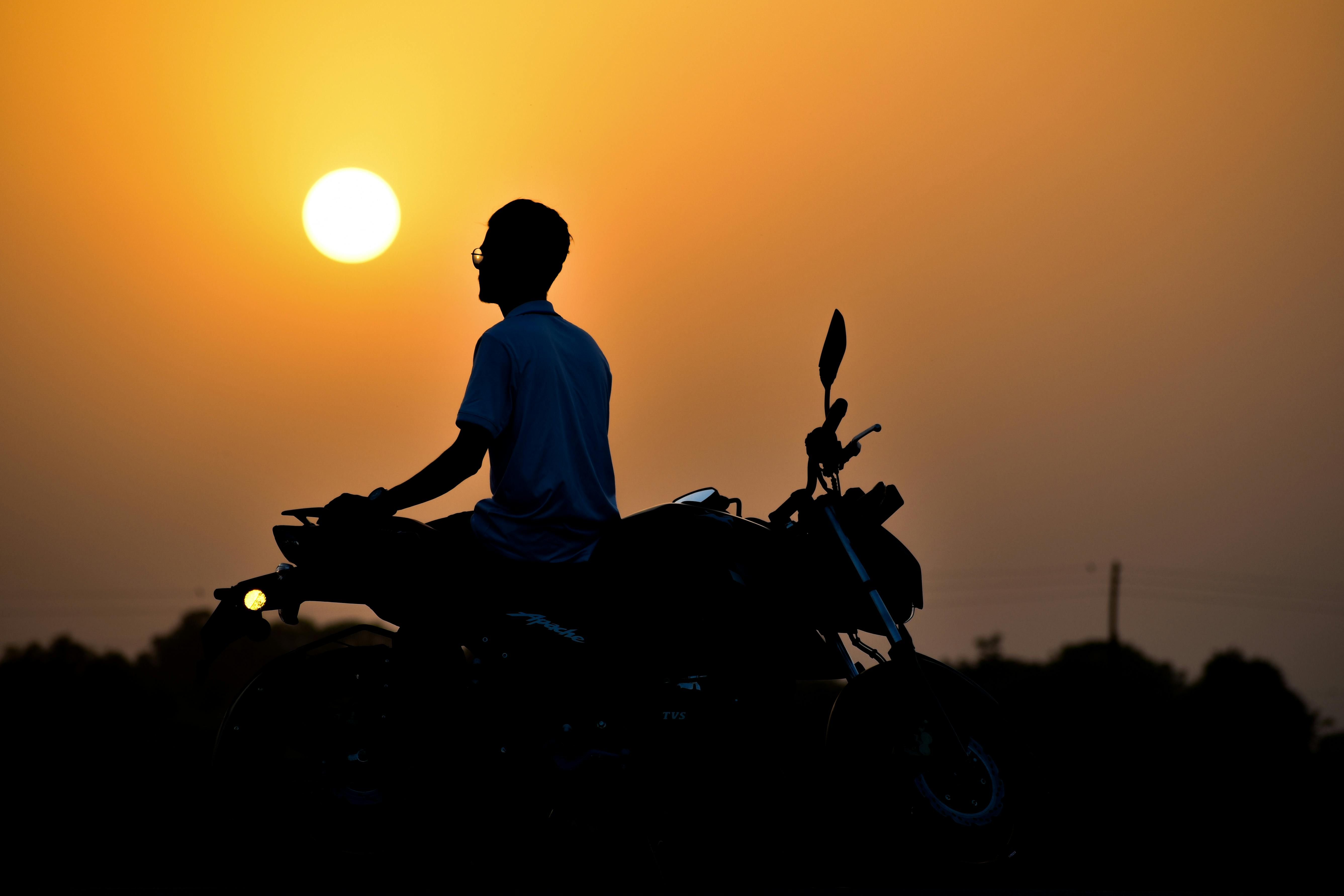 A motorcyclist enjoys a tranquil sunset ride in rural India, captured in serene silhouette.