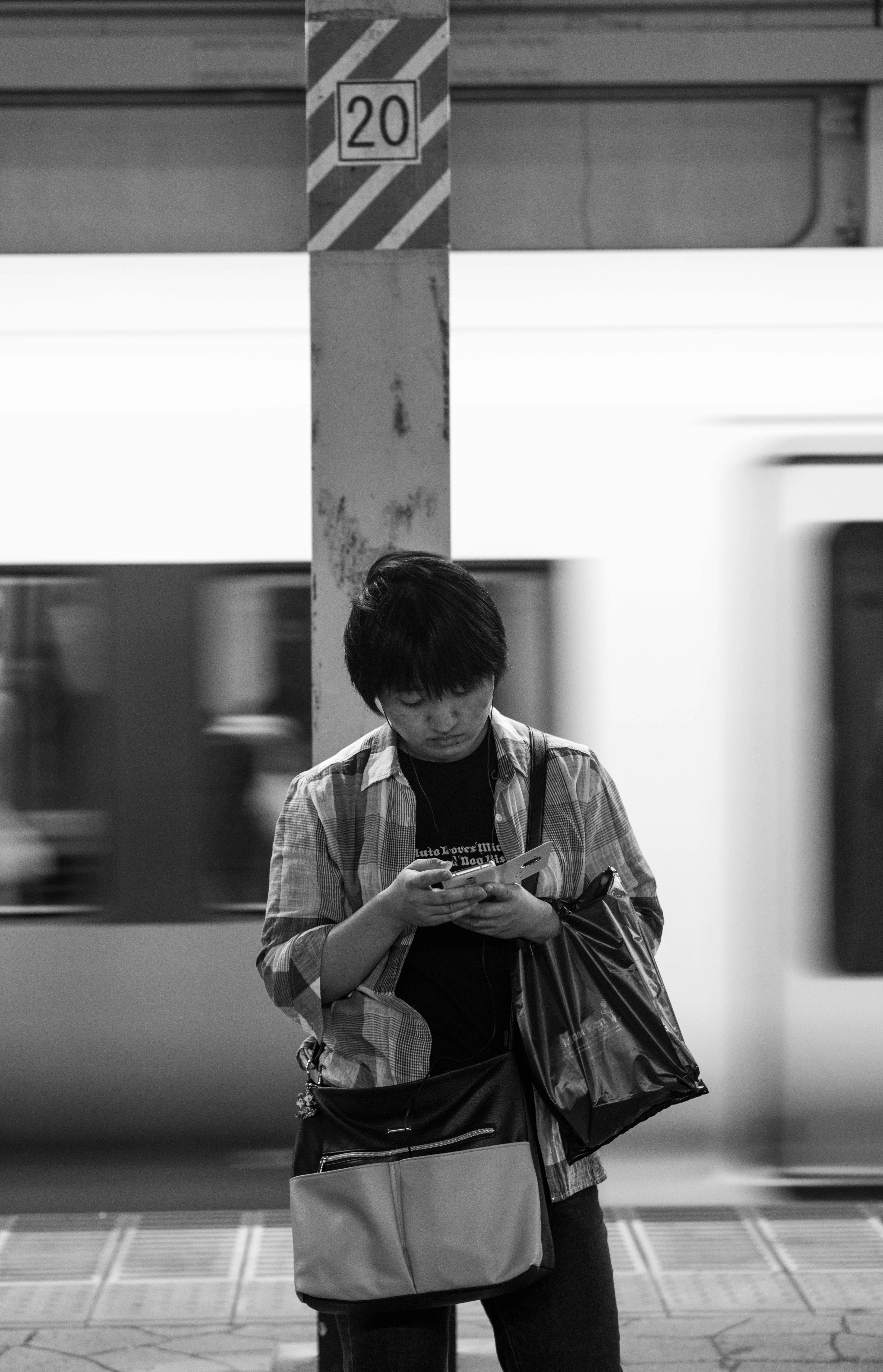 Black and white photo of a man texting at a Tokyo subway station.