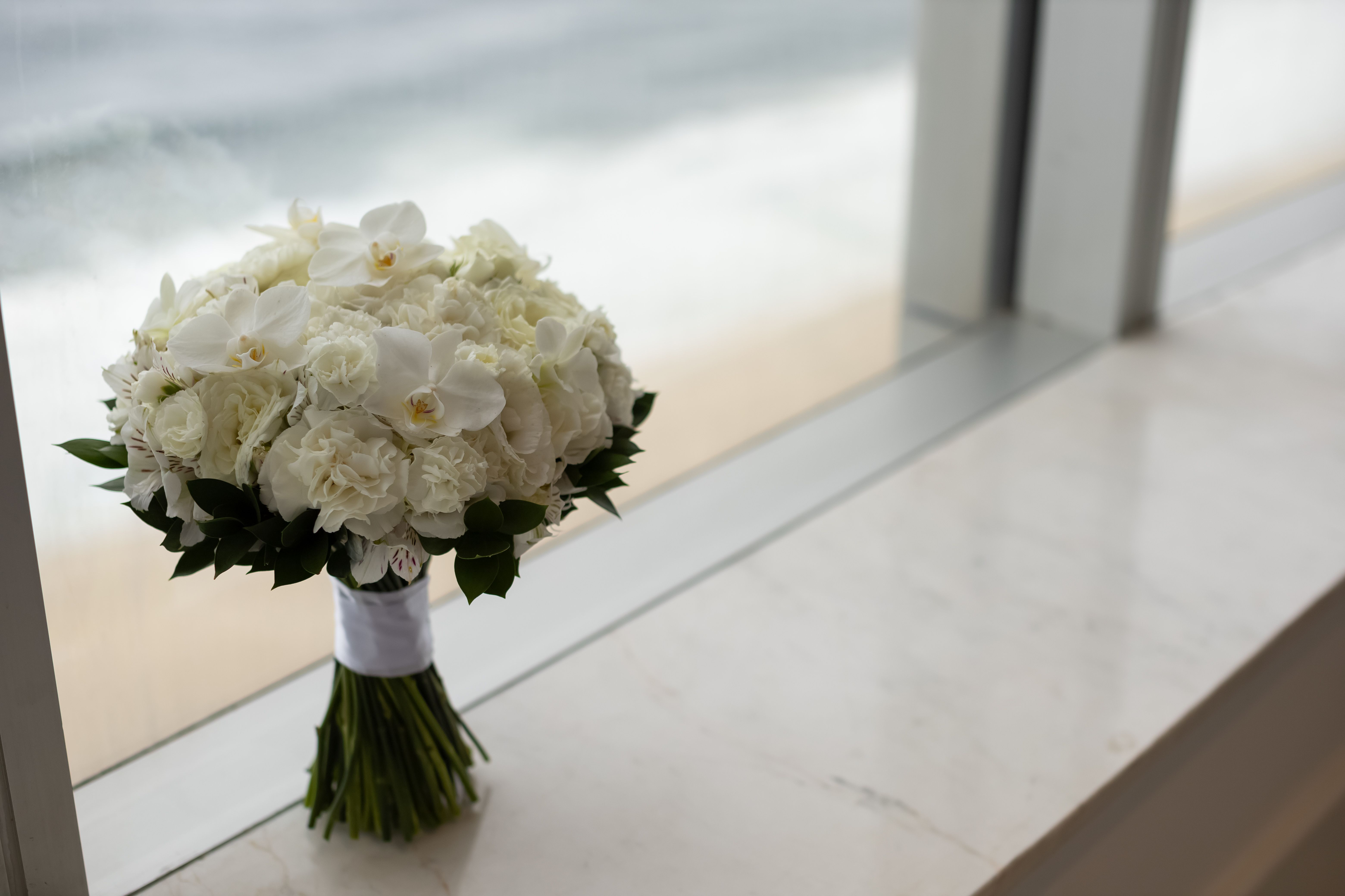 Beautiful white bouquet of roses and orchids on a marble windowsill by the sea.