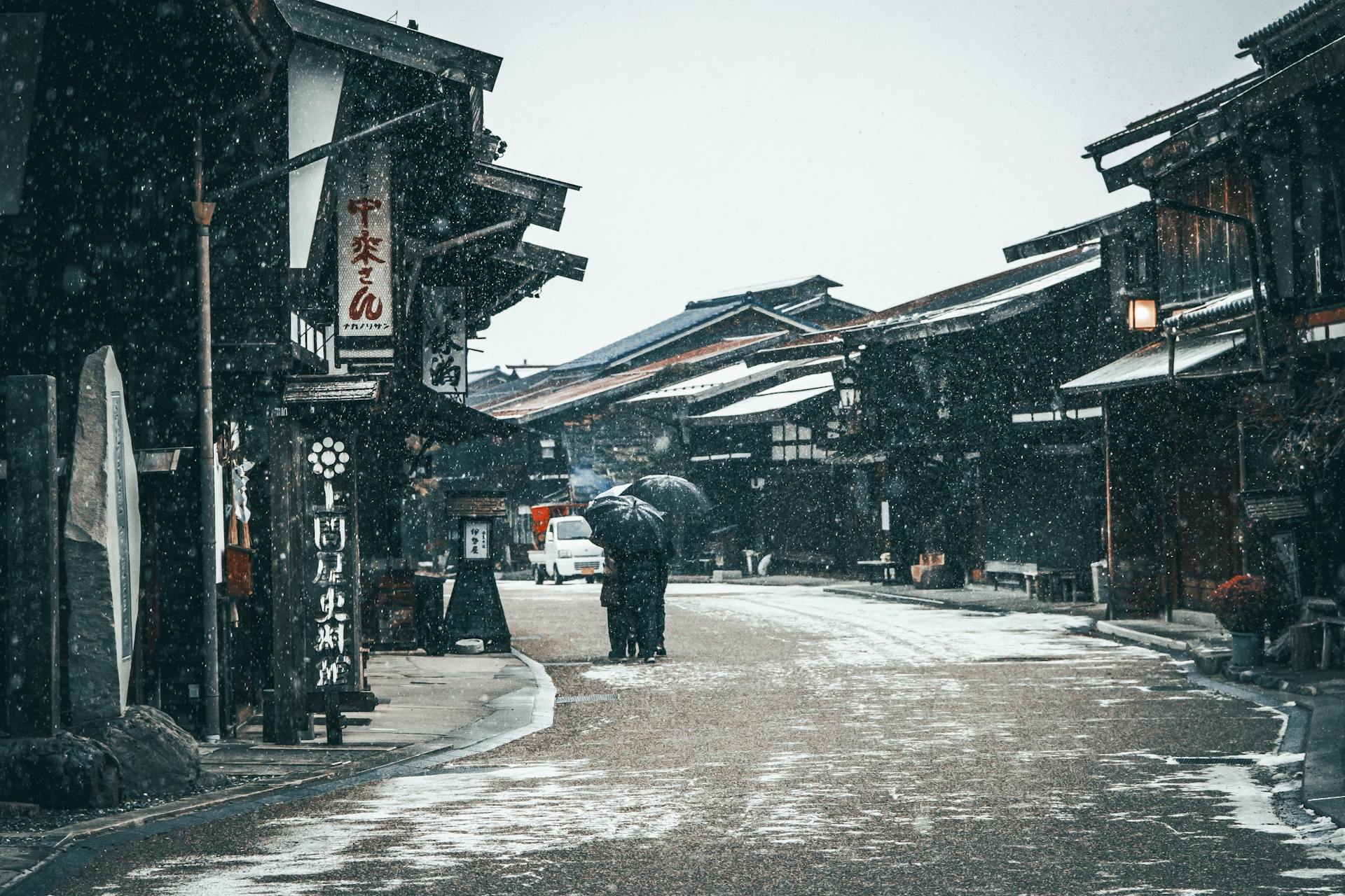 A snowy day in a historic Japanese village with traditional wooden houses and people walking with umbrellas.