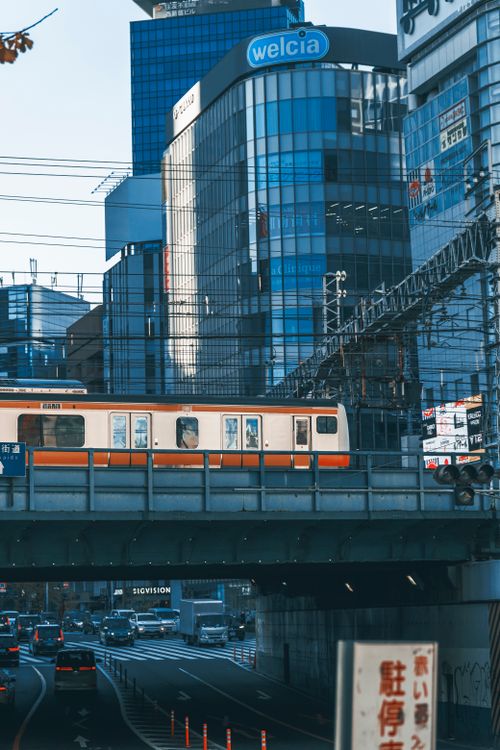 Free An orange train crosses a bridge in a bustling cityscape surrounded by glass skyscrapers. Stock Photo
