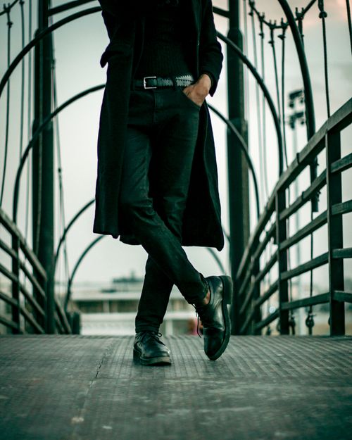 Free Fashionable man wearing long coat and shoes, posing on a contemporary bridge during the day. Stock Photo
